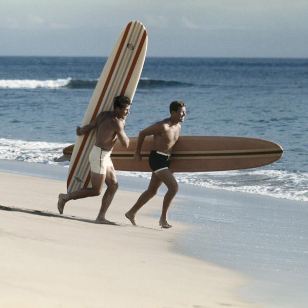 Young men running on beach with surfboard Discount